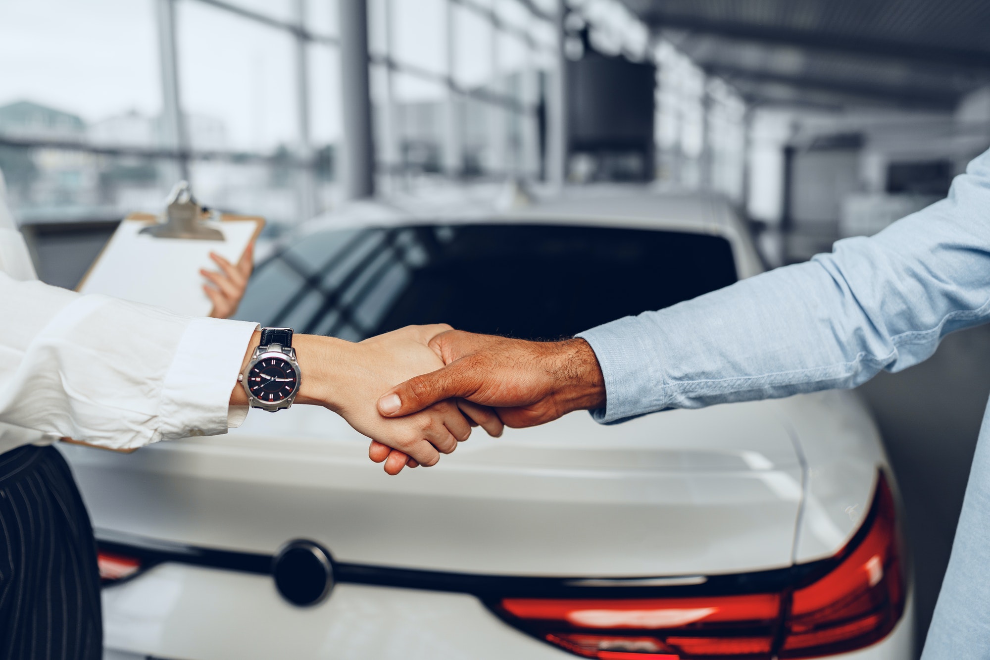 Woman car seller and man car buyer handshaking in car salon